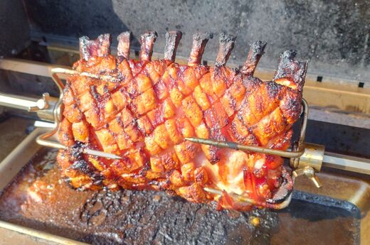 Spanferkelkrone mit Schwarte auf der Rotisserie eines Gasgrills.
